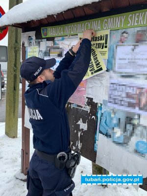policjant wiesza plakat na tablicy