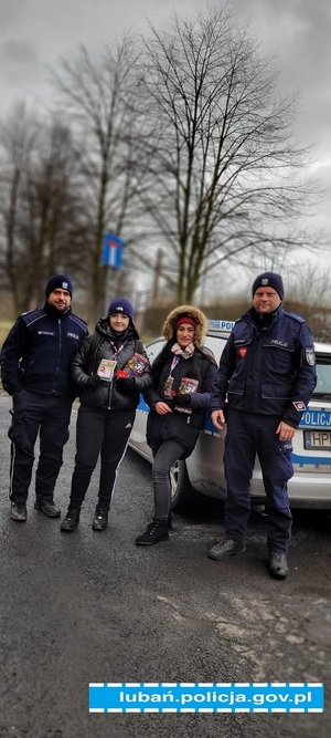 umundurowani policjanci wraz z wolontariuszkami stoją obok radiowozu