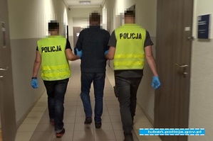 dwóch nieumundurowanych policjantów prowadzi korytarzem osobę podejrzewaną