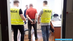 dwóch policjantów w kamizelce z napisem policja stoi przy podejrzanym trzymającym ręce z tyłu