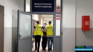 dwóch policjantów prowadzi korytarzem osobę zatrzymaną