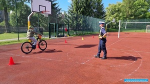 policjant stoi na płycie boiska obok jedzie uczeń na rowerze