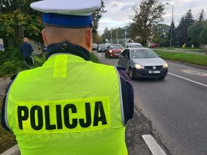 policjant umundurowany stojący tyłem posiada na kamizelce napis policja