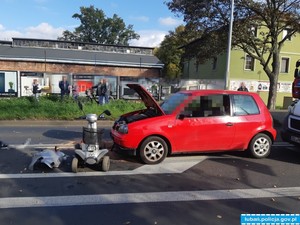 czerwone auto osobowe z podniesioną pokrywą silnika, przed autem uszkodzony w wyniku zdarzenia drogowego wózek inwalidzki z napędem elektrycznym