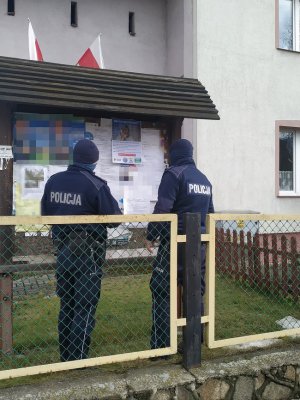 Dwóch umundurowanych policjantów stoi przy tablicy ogłoszeń a na niej widnieje plakat o bezpieczeństwie seniorów