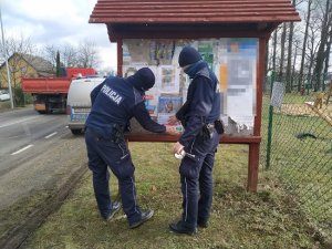 Dwóch dzielnicowych wiesza plakat na tablicy ogłoszeń informujący o bezpieczeństwie