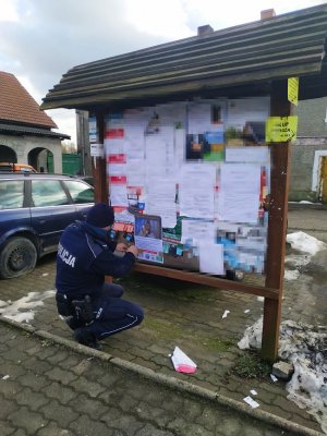 Dzielnicowy wiesza plakat na tablicy ogłoszeń